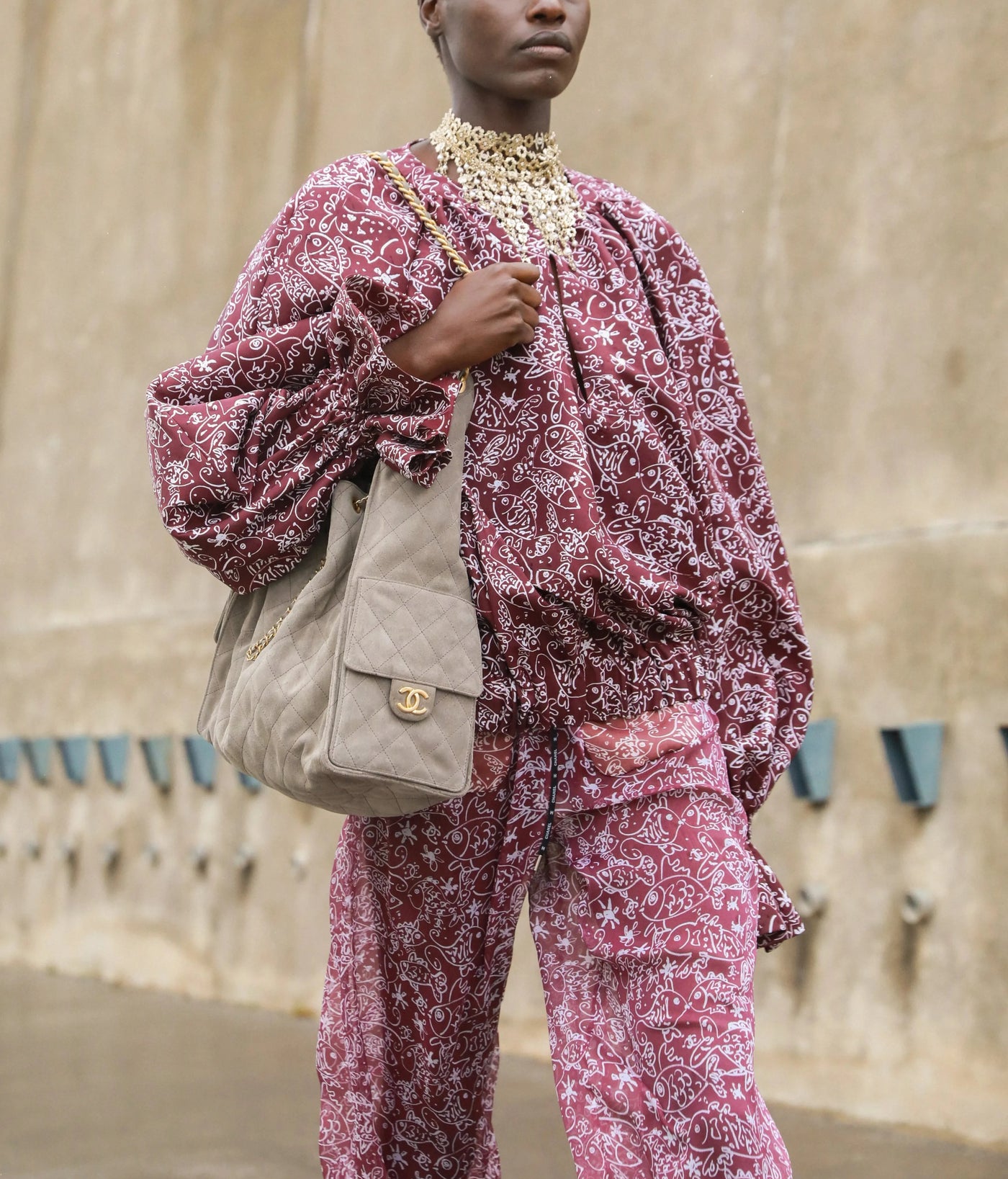 Person wearing a pink floral outfit with a beige Chanel 25 bag against a beige wall. The CHANEL bag is for sale;